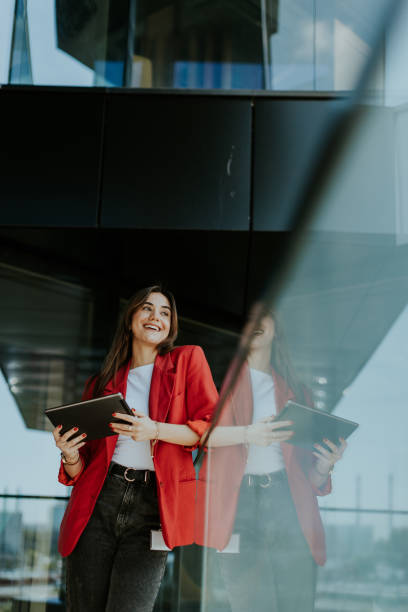 istock Smiling businesswoman in red blazer using tablet at modern office window in daylight 2157254239