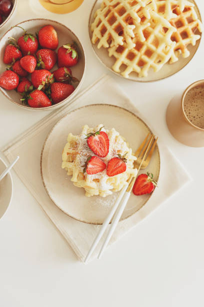 Belgian waffles with strawberries and powdered sugar on white table. Summer food concept. Soft focus