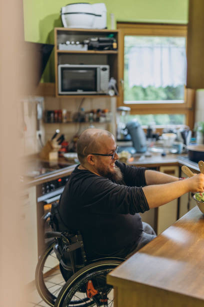 istock Young Disabled Man Sitting On Wheel Chair Preparing Food In Kitchen 2157266888