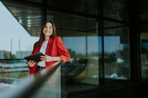 istock Smiling businesswoman in red blazer using tablet at modern office window in daylight 2157268012