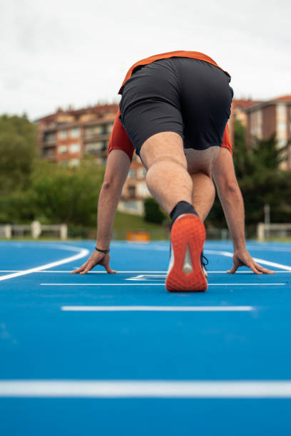 istock vertical Runner Crouched at Starting Line Ready to Begin Race on Blue Athletic Track 2157271702