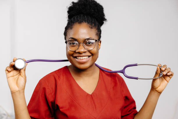 Smiling Female Doctor Holding Stethoscope A smiling female doctor in a red scrubs, with glasses, holds a stethoscope. red medical scrubs stock pictures, royalty-free photos & images