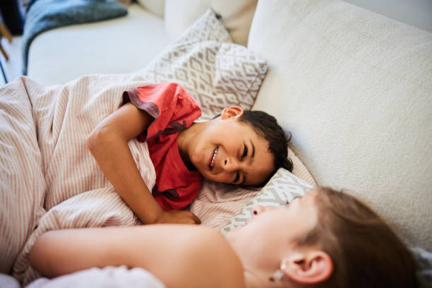 istock Laughing little boy lying with his older sister on a sofa at home 2157273807