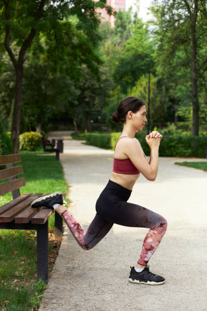fitness woman doing squats exercise with a bench in a park