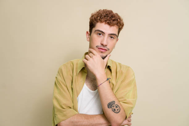 istock Thoughtful young man with hand on chin posing on beige background 2157278487