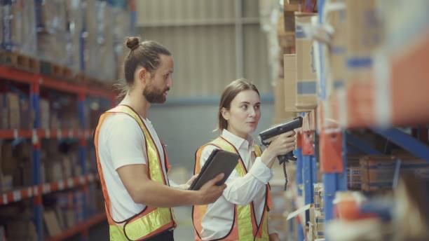 Warehouse employees check items according to program to be shipped on tapelets with goods packed into cartons on pallets and arranged on shelves in a large and modern warehouse. Stock management, online delivery system, logistics, transportation. Warehouse employees check items according to program to be shipped on tapelets with goods packed into cartons on pallets and arranged on shelves in a large and modern warehouse. Stock management, online delivery system, logistics, transportation. order preparation system logistic stock pictures, royalty-free photos & images