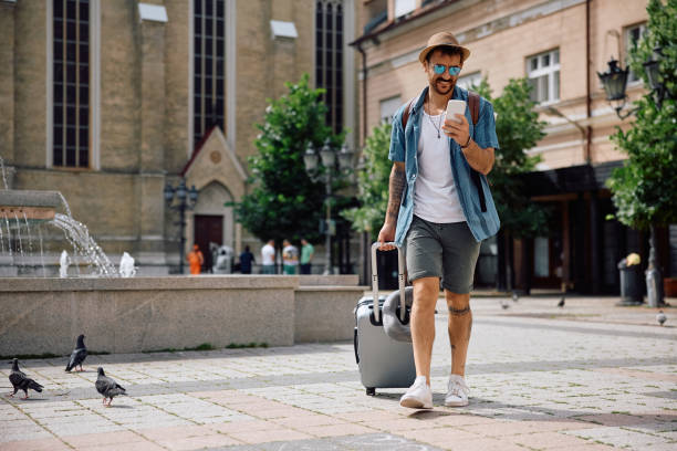 istock Happy traveler using mobile phone while walking with a suitcase on the street. 2157291732