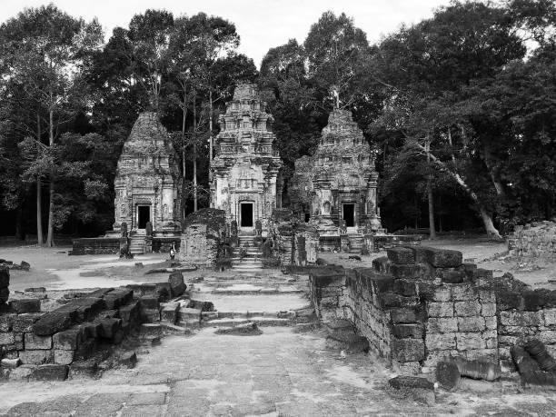 Black and white photo of ancient temple ruins surrounded by trees. The temple structures are made of stone and show signs of wear and age.