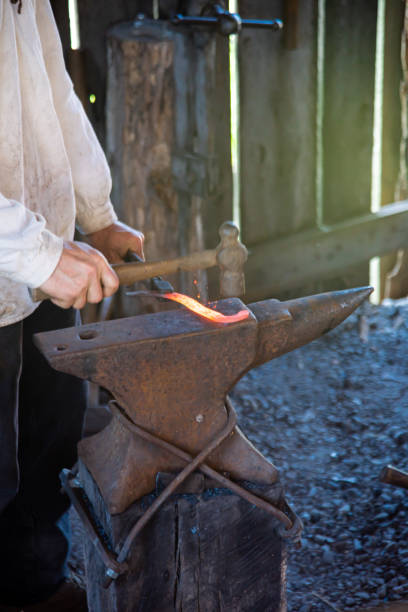 istock Blacksmith man hand using hammer to forge cast iron melting on medieval anvil traditional trade workshop, Mansfield, Missouri, anvil with smooth working surface of hardened steel strike forging 2157295038