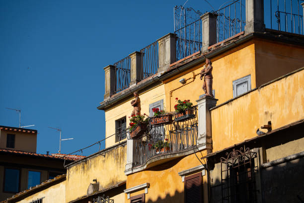 Sunlight bathes an inviting balcony in Florence, Italy, adorned with statues and plants, reflecting typical Italian urban landscape