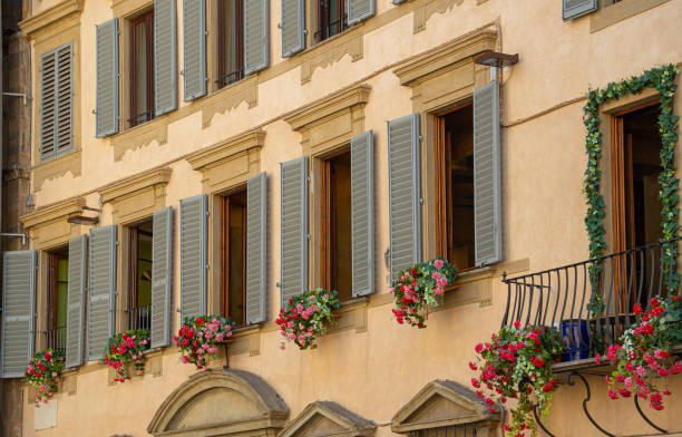 A picturesque facade of a Florentine building decorated with green shutters and vibrant flower boxes in Italy