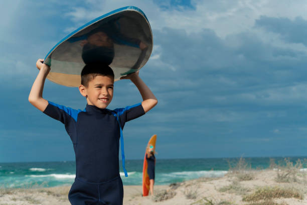 Portrait of little surfer boy with bodyboard have fun on beach, walk by white sand beach. Summer adventures, active families, parents and kids lifestyle, sports activities on school holiday with kids