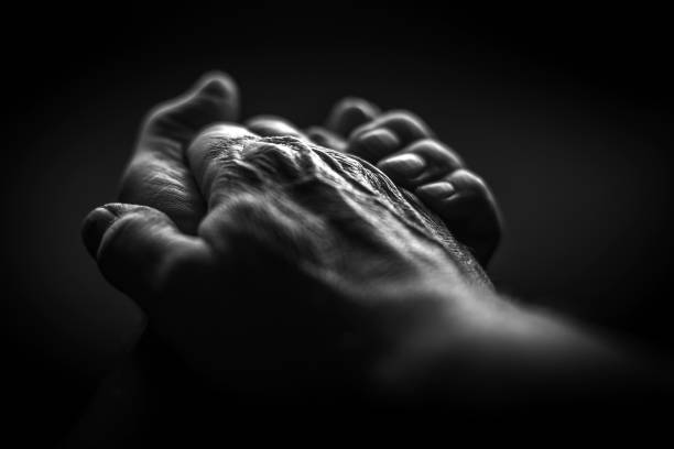 Black and white. Wrinkled hands folded together on a black background
