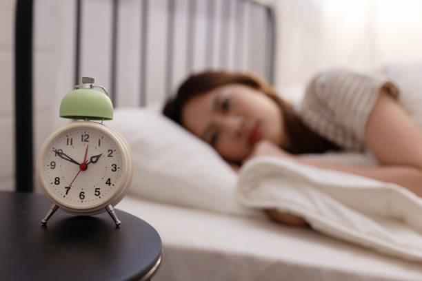 istock Asian woman suffer from insomnia  with a clock on bed side 2157320203