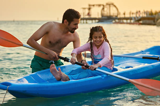 Shirtless man assisting daughter sitting on kayak Shirtless father assisting daughter sitting on kayak in sea at sunset half dressed girls pictures stock pictures, royalty-free photos & images