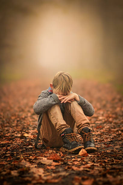 istock Sad yound blond boy sitting on  Forest floor branch in the woods. 2157330848
