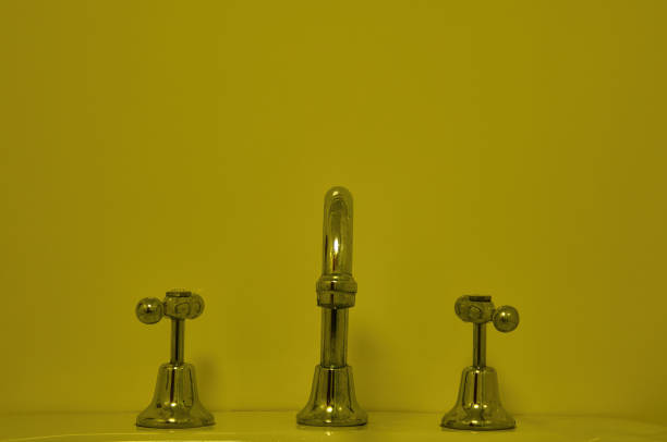 Shiny chrome vintage faucet with two taps and a smooth yellow-green background