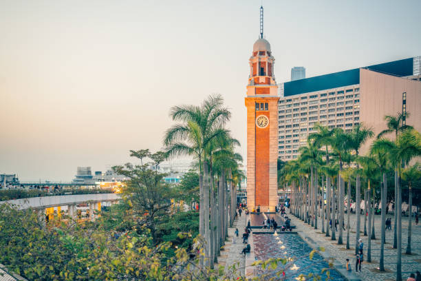 Elegant view of the historic Clock Tower surrounded by palm trees at dusk in Hong Kong, China. People strolling and relaxing in the serene urban environment.