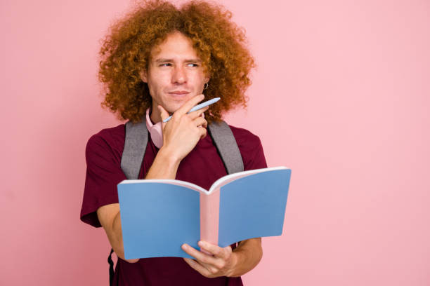 Young college student with a backpack and headphones is deep in thought, holding a notebook and pen while contemplating a question