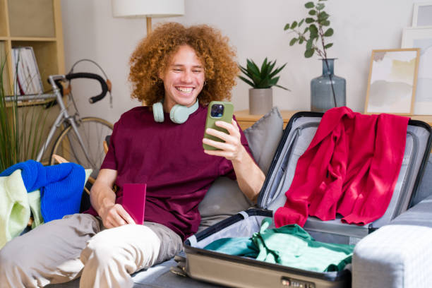 istock Happy tourist using smartphone while packing suitcase for travel 2157349341