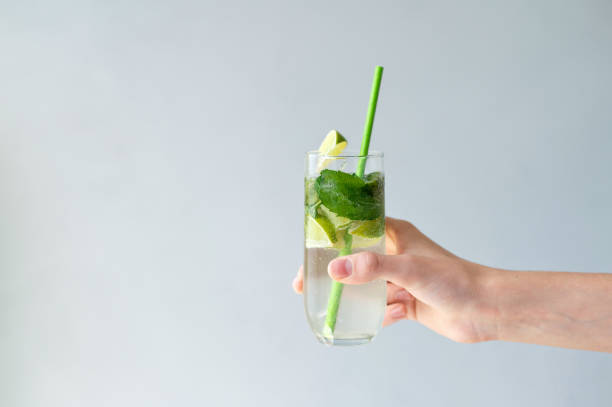 istock Hand holding glass with iced refreshing mojito cocktail drink on light blue neutral background with empty copy space 2157353279