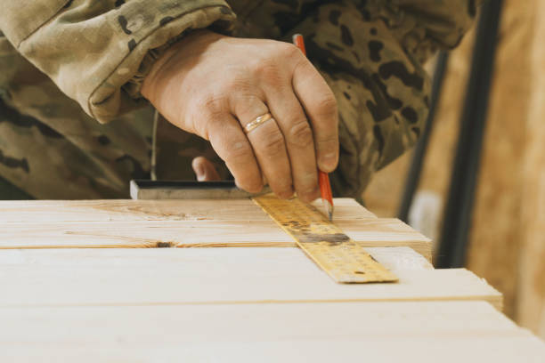 A close-up view of a carpenters hands using a pencil and ruler to mark precise measurements on a wooden board during a woodworking project.