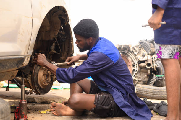 In a Nigerian workshop, a mechanic is carefully removing a faulty brake pad from a vehicle, ensuring precise handling to maintain safety and performance on the road.