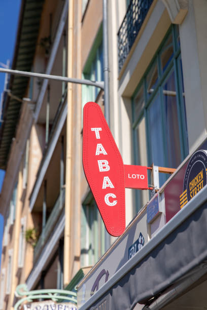 Nice, France - June 12, 2024: A bright red Tabac sign displayed outside a local tobacco shop in Nice. The sign is mounted on a cream-colored building with large windows and light blue frames, typical of the architectural style in the area