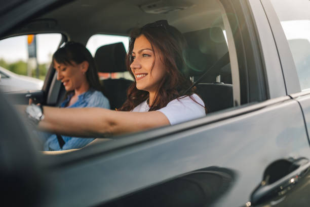 istock Cheerful young woman driving a car while her friend using a cellphone. 2157364591