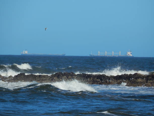 istock waves breaking on rocks with ships in the background 2157365566