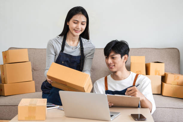 istock Young Couple Managing Their Small Online Business from Home, Packing Boxes and Using Laptop for Inventory and Orders 2157374395