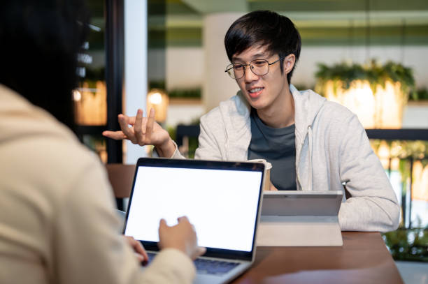 istock A happy Asian male student is talking with his friend while doing homework together in a cafe. 2157382394