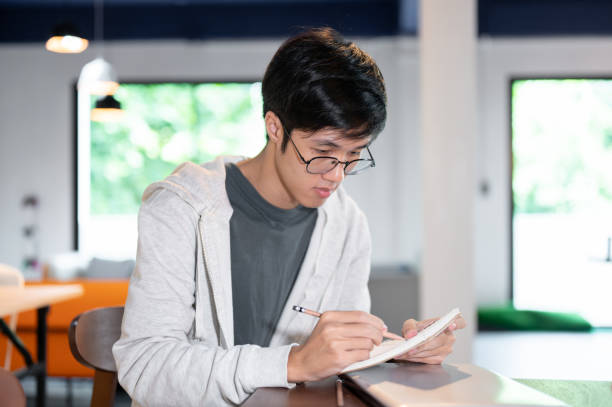 istock Smart Asian male college student is taking notes in his notebook or doing homework in a coffee shop. 2157382491
