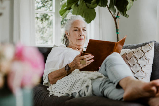 istock Elderly woman reading a book on a sofa in a weekend 2157383343