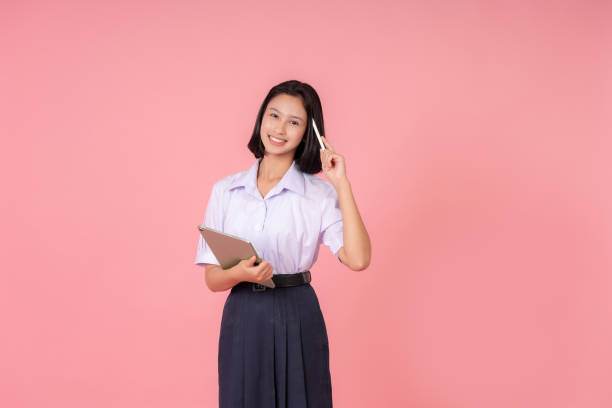 istock Asian female high school student smiling cutely and holding a laptop, using a pen, thinking about education and studying online, taking pictures in a pink studio background. 2157392269