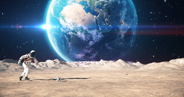 Young Astronaut On An Alien Planet Playing Soccer. Shooting Slowly. Planet Earth Is Visible. Space Related Majestic Scene.World Map Credits To NASA : https://visibleearth.nasa.gov/images/57752/blue-marble-land-surface-shallow-water-and-shaded-topography