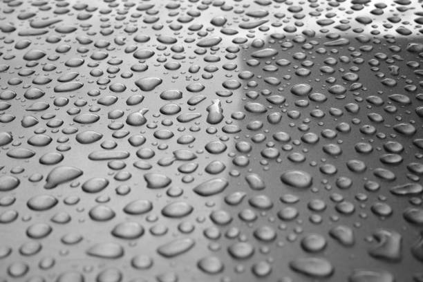 A close-up photograph of water droplets on a red car surface. The droplets create a vibrant and reflective pattern, highlighting the smooth, polished paint of the car. The image captures the contrast between the glossy red surface and the irregular shapes of the water droplets, emphasizing the fresh, clean effect after rainfall or washing