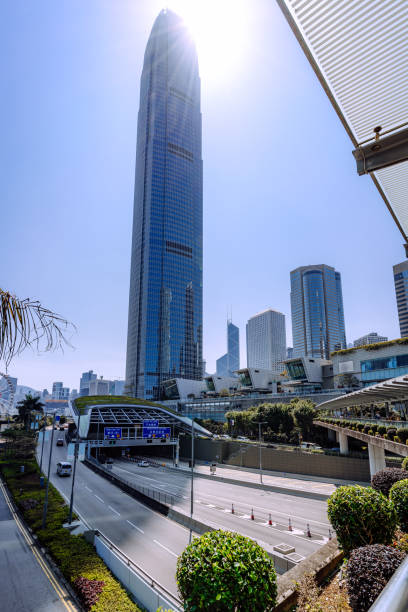 A striking skyscraper against a sunny sky in Hong Kong's bustling business district, showcasing modern architecture and a vibrant urban scene.