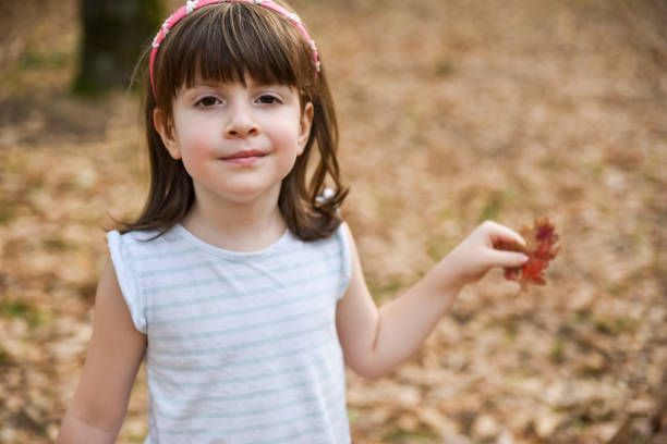A young child wearing a cozy yellow hat holds a handful of colorful autumn leaves in a park, enjoying the beauty of fall foliage and the joy of nature.