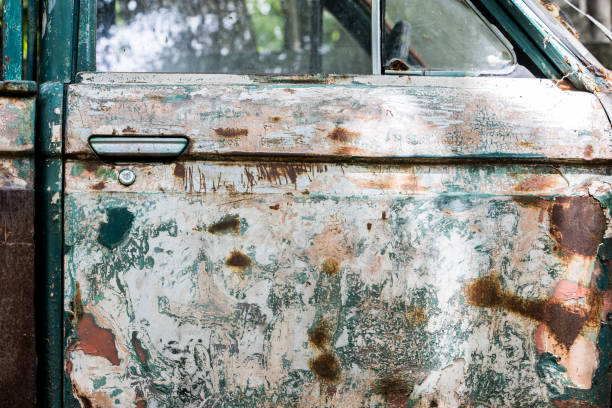 Side view of an old olive-green car, paint peeling, rough, and erosion on the surface of the car door. Vintage car.
