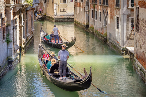 Venice, Italy - June 5th 2024: Gondola with tourists in a broad channel in the old town of Venezia - the striped shirt is a uniform for the gondoliers
