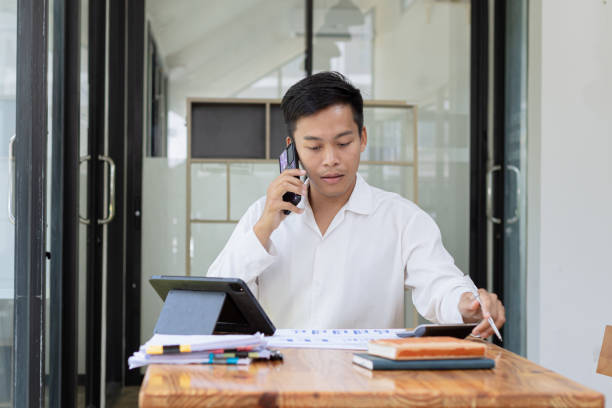 istock Asian businessman using smartphone with paperwork at office desk. 2157403898