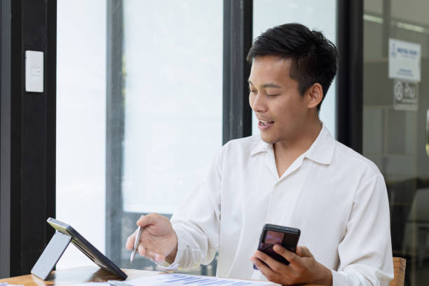 istock Asian businessman using smartphone with paperwork at office desk. 2157403899