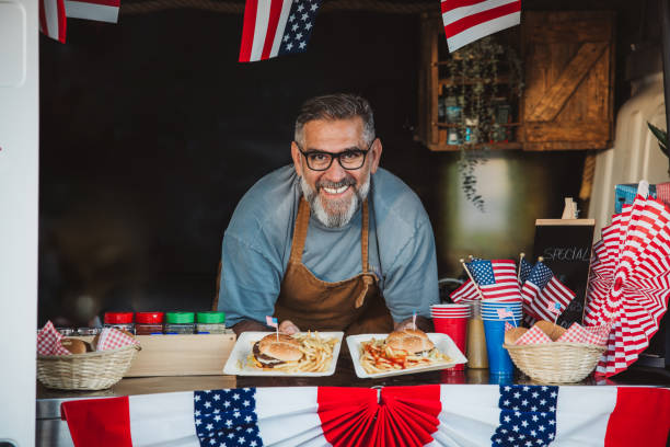 Food truck owner poses at the bar of his business. Truck is decorated with flags for fourth of July.