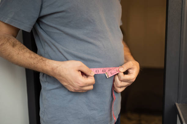 A man measures his abdomen with a measuring tape Overweight man measures his waist with measuring tape. Fat belly visceral fat. Body mass index, grade 1 obesity, eating disorders and physical activity, excess high-calorie food or eating disorder excess fat stock pictures, royalty-free photos & images