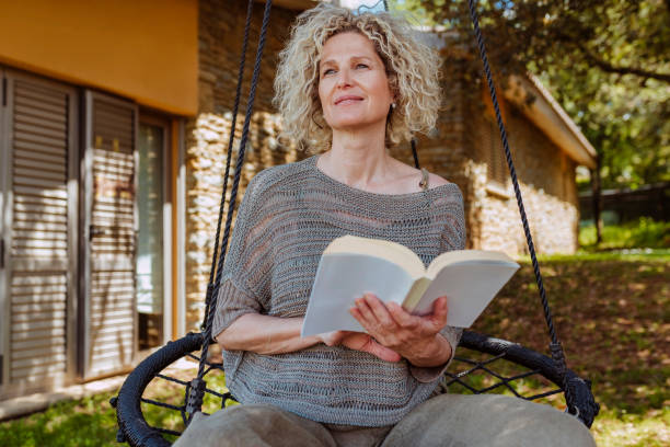Smiling middle aged woman reading a book in hammock