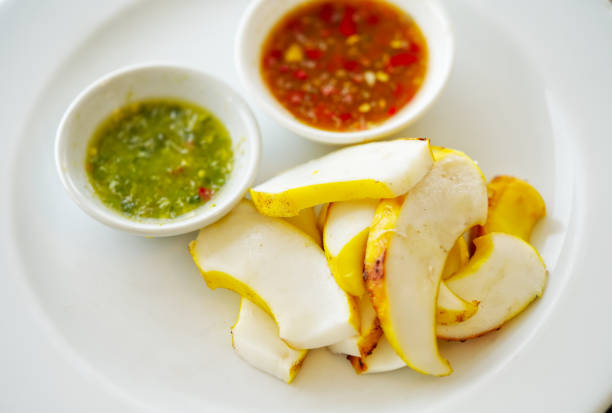 Close up grilled sliced squid on a white plate with two style of sauce, seafood and sweet chili sauce. Thai food style of grilled marinated squid. Natural light, view from above.