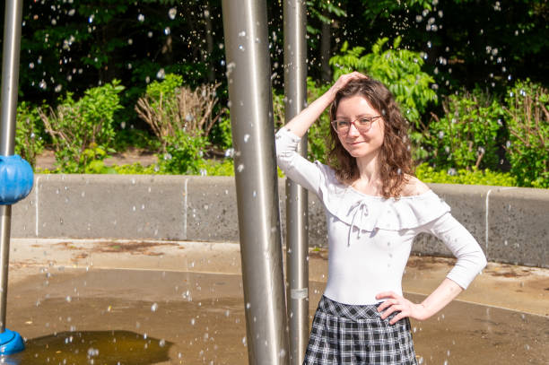 Young woman in water play with water dropping all around her in playground during summer day