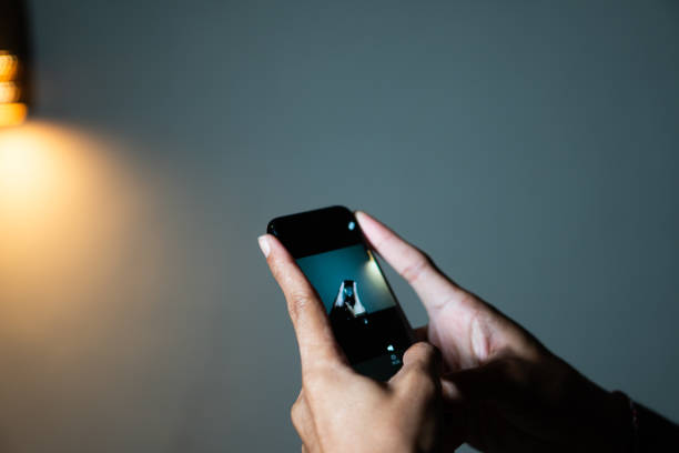 Close-up of hands holding a smart phone and taking a photo in a dimly lit room.
