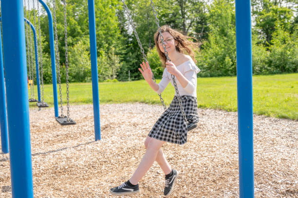 Young woman sitting on swing in playground during summer day